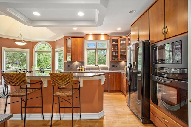 kitchen with brown cabinets, a raised ceiling, light wood-style floors, a sink, and black appliances