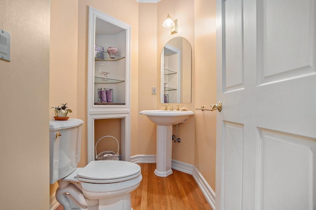 half bathroom with built in shelves, toilet, baseboards, and wood finished floors