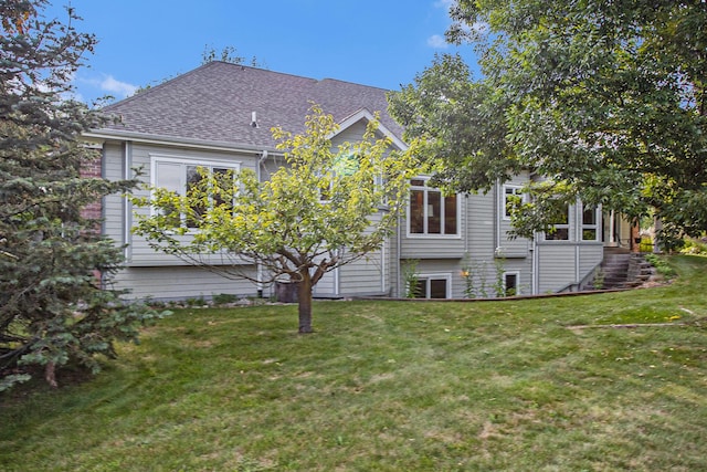 back of property with roof with shingles and a lawn