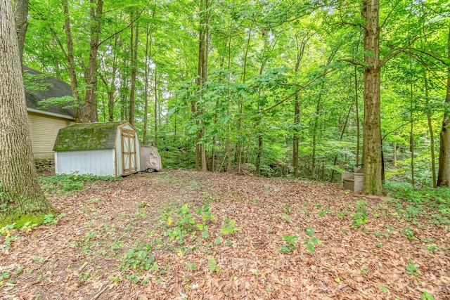 view of yard with a storage unit, a wooded view, and an outbuilding