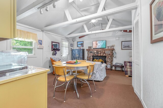 dining room with rail lighting, lofted ceiling with beams, a stone fireplace, and carpet flooring