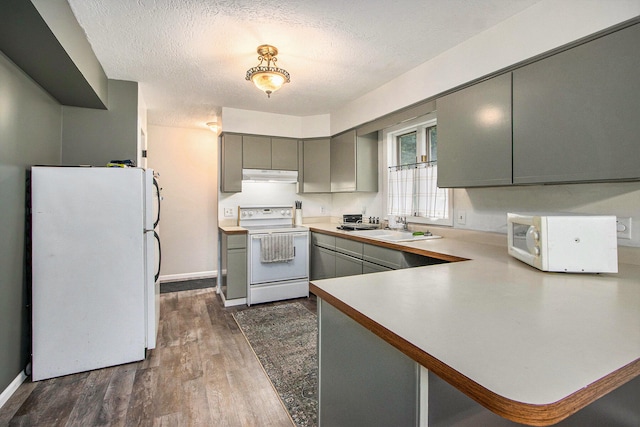 kitchen with dark hardwood / wood-style floors, sink, kitchen peninsula, a textured ceiling, and white appliances