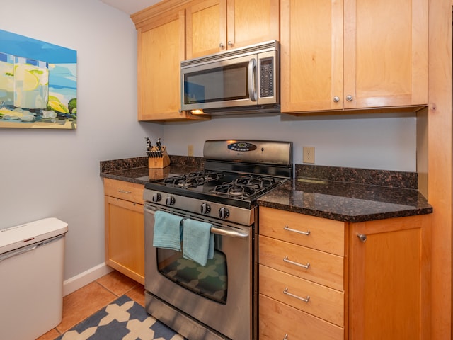 kitchen featuring dark stone countertops, light tile patterned floors, stainless steel appliances, and light brown cabinetry