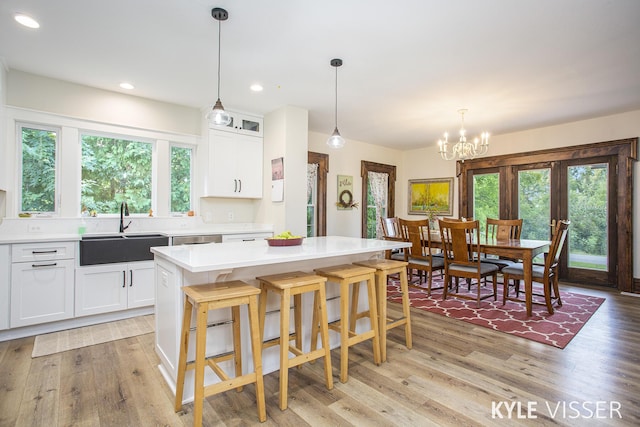 kitchen with light wood finished floors, a breakfast bar, light countertops, white cabinetry, and a sink