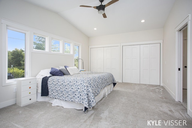 bedroom featuring lofted ceiling, multiple windows, two closets, and light colored carpet