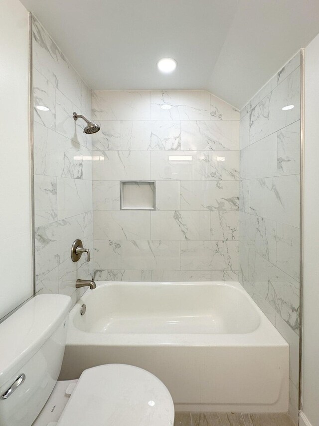 bathroom featuring toilet, tiled shower / bath, and vaulted ceiling