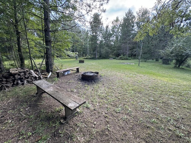 view of property's community with a yard, a view of trees, and an outdoor fire pit