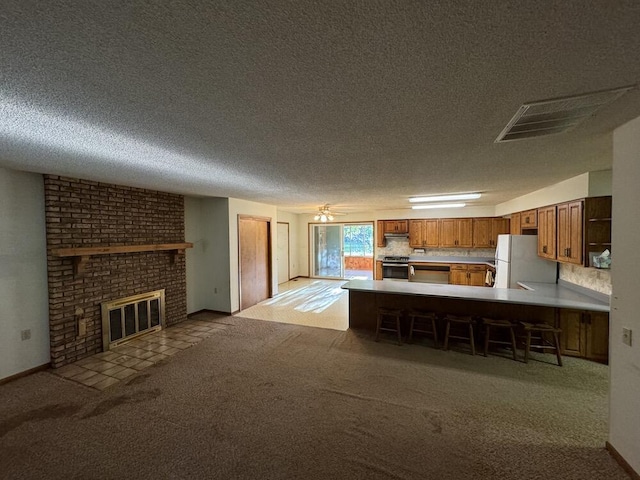 kitchen with brown cabinetry, visible vents, freestanding refrigerator, light countertops, and electric stove