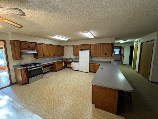 kitchen featuring under cabinet range hood, light floors, brown cabinets, white appliances, and a sink