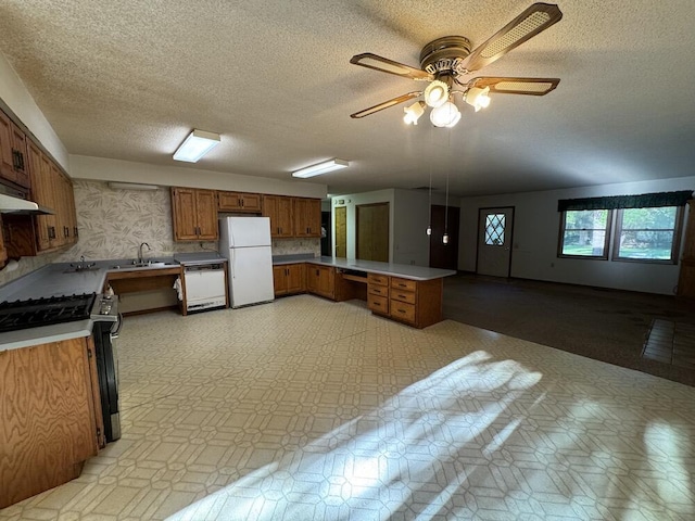 kitchen with brown cabinets, a sink, white appliances, a peninsula, and light floors