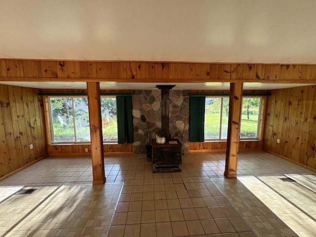 unfurnished living room featuring tile patterned floors, visible vents, wood walls, and a wood stove