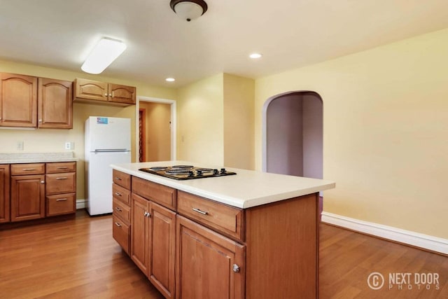 kitchen featuring black gas cooktop, white fridge, a kitchen island, and wood-type flooring