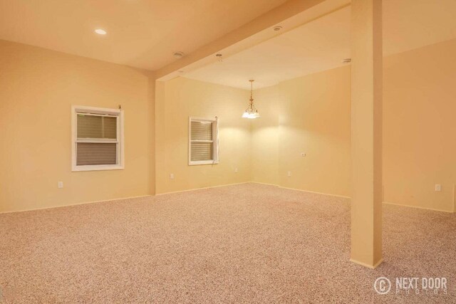 carpeted empty room featuring an inviting chandelier and beam ceiling