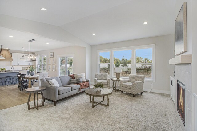 living room featuring lofted ceiling, light hardwood / wood-style flooring, a notable chandelier, and a tile fireplace