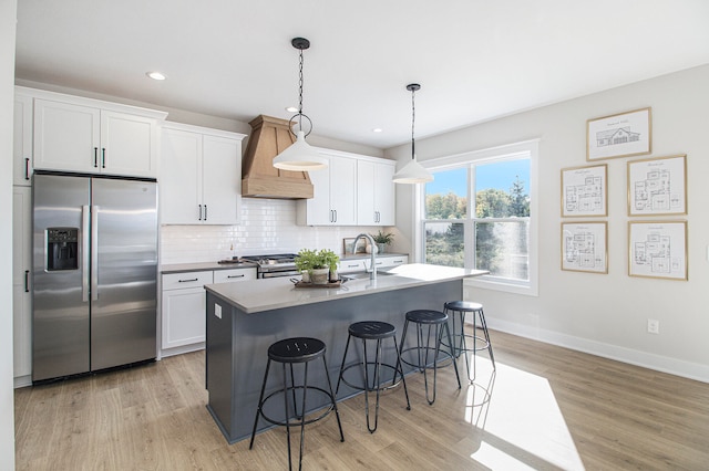 kitchen featuring light wood-type flooring, stainless steel appliances, custom exhaust hood, white cabinetry, and a kitchen island with sink