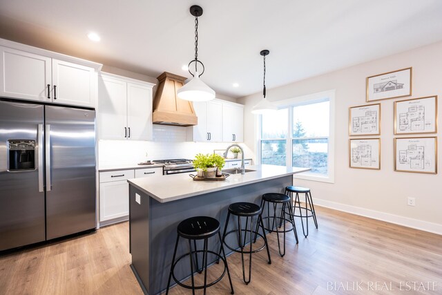 kitchen with a center island with sink, premium range hood, appliances with stainless steel finishes, and light hardwood / wood-style floors