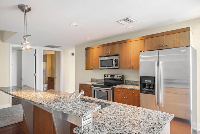 kitchen with stainless steel appliances, visible vents, decorative light fixtures, and an island with sink