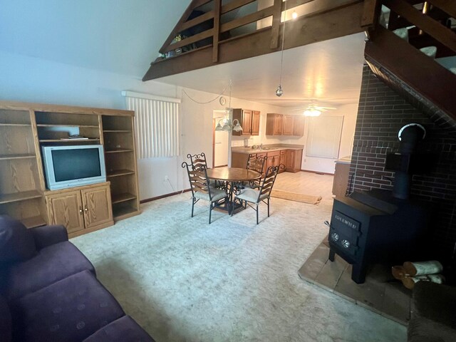 carpeted living room with high vaulted ceiling, ceiling fan, and a wood stove