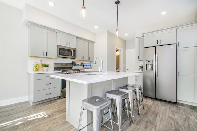 kitchen featuring light wood-type flooring, stainless steel appliances, sink, decorative light fixtures, and a center island with sink