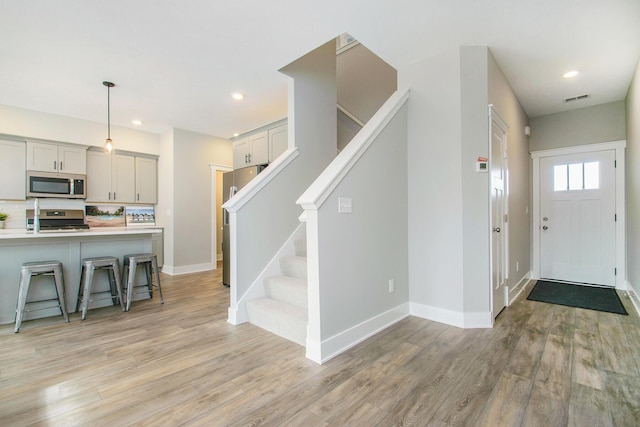 foyer with light wood finished floors, baseboards, stairs, and visible vents