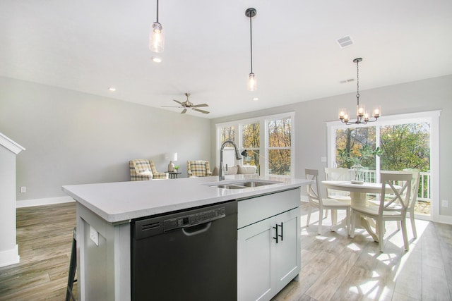 kitchen with black dishwasher, light countertops, light wood-style flooring, a kitchen island with sink, and a sink