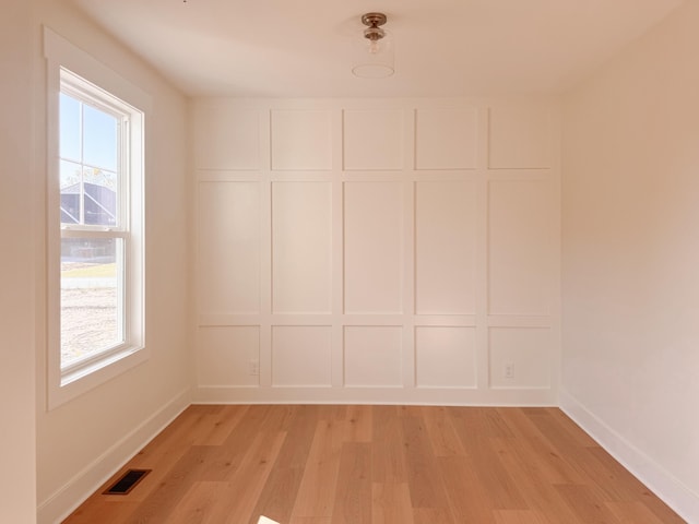 spare room featuring baseboards, visible vents, a decorative wall, and light wood finished floors