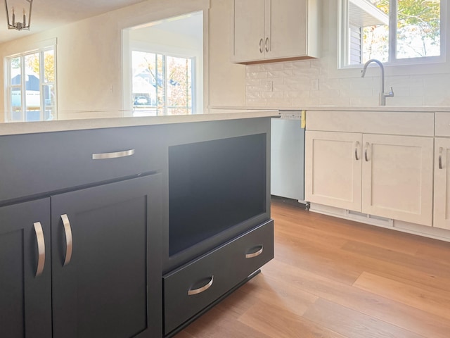 kitchen with light countertops, stainless steel dishwasher, white cabinets, and light wood-style floors