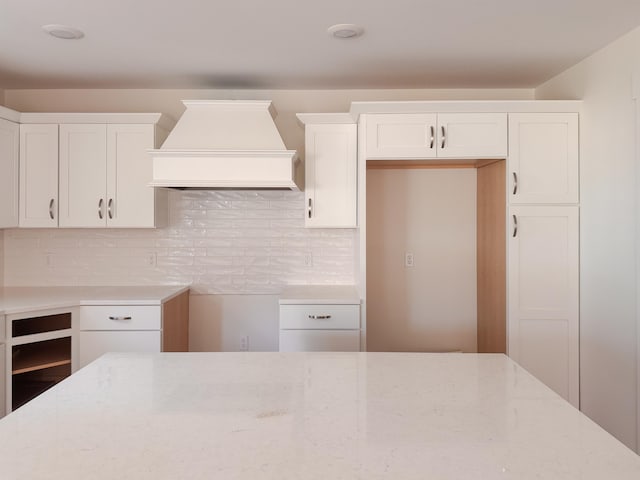 kitchen with tasteful backsplash, custom exhaust hood, white cabinetry, and light stone countertops