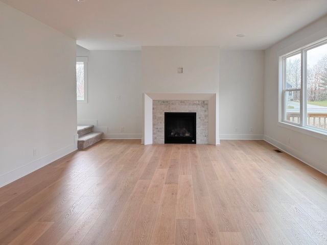 unfurnished living room featuring visible vents, a fireplace, light wood-style flooring, and baseboards