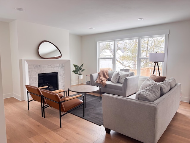 living room with light wood-type flooring, baseboards, and a glass covered fireplace