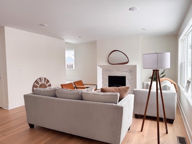 living area with light wood-type flooring, baseboards, visible vents, and a tiled fireplace