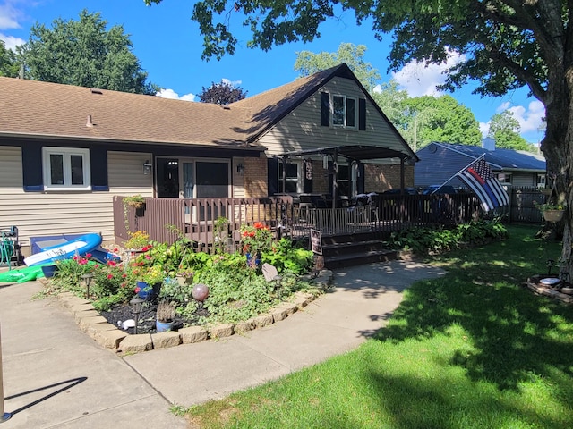 view of front of home featuring brick siding, a shingled roof, fence, a front yard, and a deck