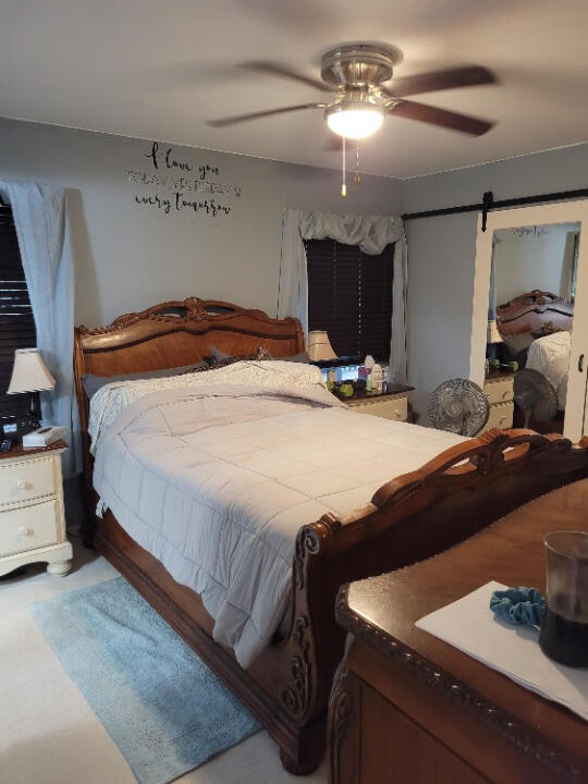 carpeted bedroom with a barn door and ceiling fan