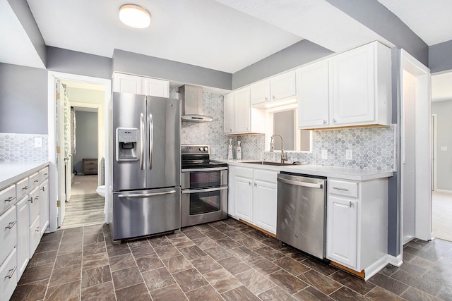 kitchen with wall chimney exhaust hood, appliances with stainless steel finishes, sink, decorative backsplash, and white cabinets