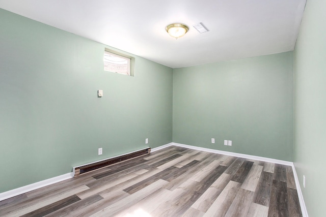 unfurnished room with a baseboard heating unit and hardwood / wood-style floors