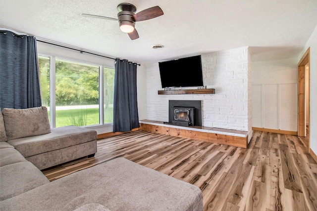 living room featuring a textured ceiling, hardwood / wood-style floors, ceiling fan, and a stone fireplace