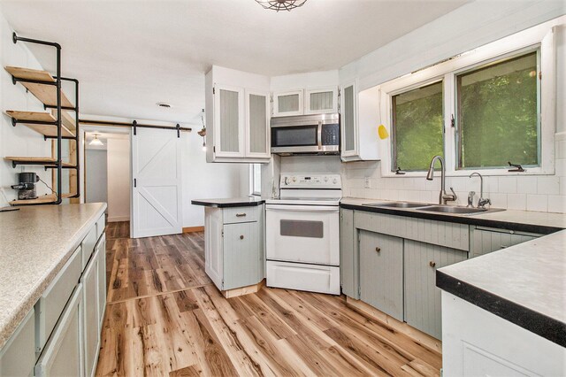 kitchen with light hardwood / wood-style flooring, white range with electric cooktop, sink, decorative backsplash, and a barn door