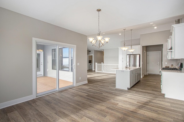 kitchen featuring white cabinets, hardwood / wood-style flooring, decorative light fixtures, stainless steel refrigerator, and a kitchen island with sink