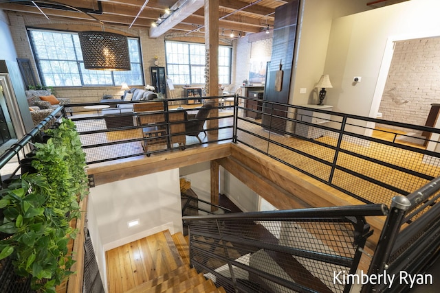 stairs featuring beamed ceiling, brick wall, and hardwood / wood-style floors