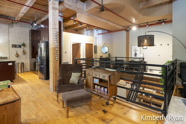 interior space featuring brick wall, light wood-type flooring, beam ceiling, and track lighting