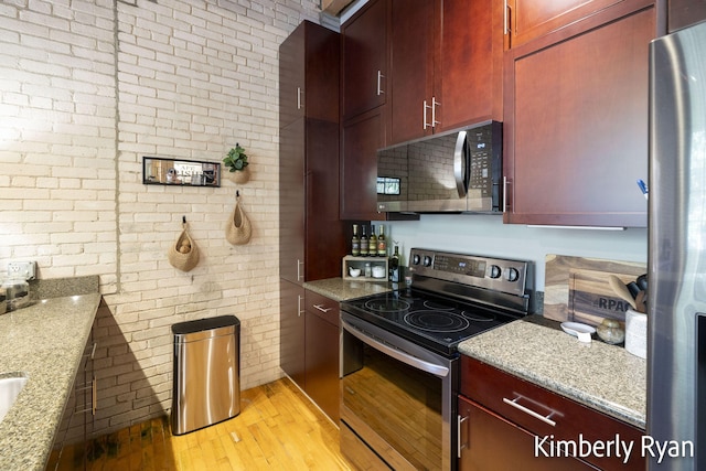 kitchen featuring appliances with stainless steel finishes, light wood-type flooring, light stone countertops, and brick wall