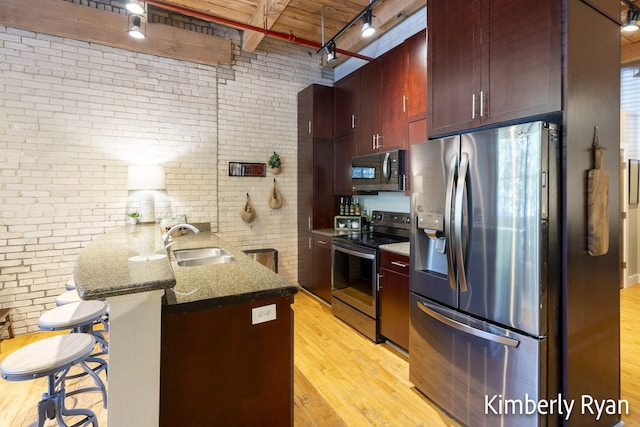 kitchen with light hardwood / wood-style floors, brick wall, kitchen peninsula, stainless steel appliances, and a kitchen bar