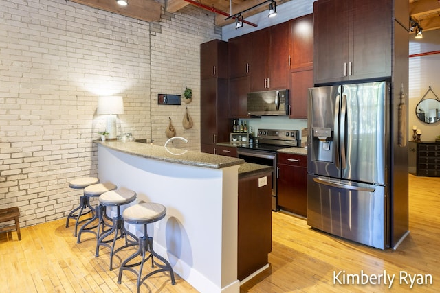 kitchen with kitchen peninsula, brick wall, stainless steel appliances, a kitchen breakfast bar, and light wood-type flooring