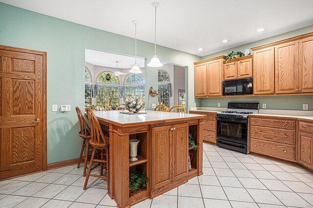 kitchen featuring black appliances, light tile patterned floors, decorative light fixtures, a kitchen island, and a kitchen bar