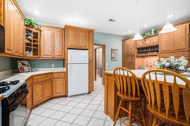 kitchen with black gas range oven, white refrigerator, pendant lighting, a breakfast bar area, and light tile patterned floors