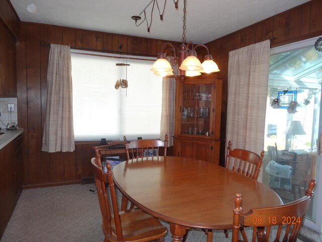 dining room featuring a notable chandelier, wooden walls, and light colored carpet