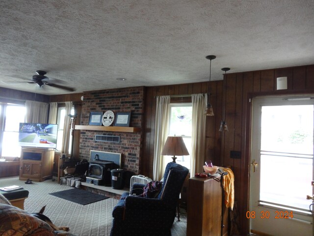 carpeted living room with a textured ceiling, wood walls, ceiling fan, and a brick fireplace