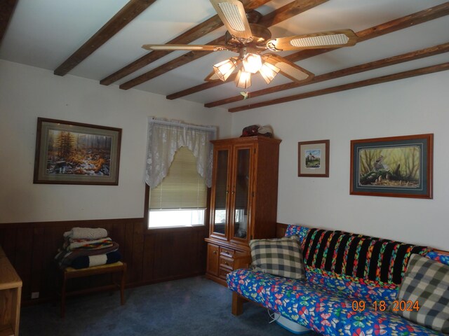 living room featuring ceiling fan, wood walls, beam ceiling, and dark carpet