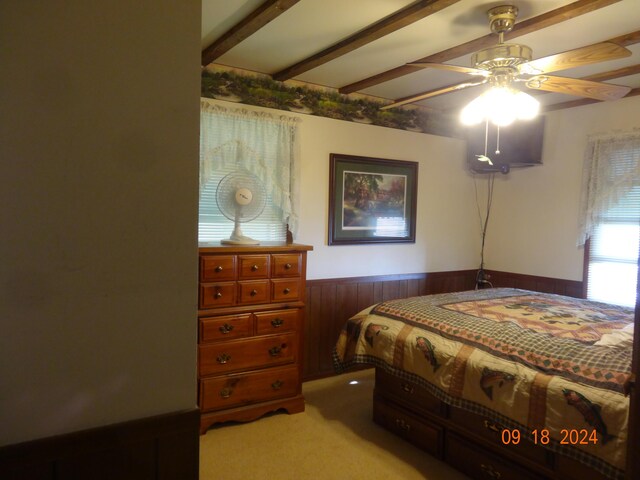 bedroom featuring beam ceiling, ceiling fan, wood walls, and light colored carpet