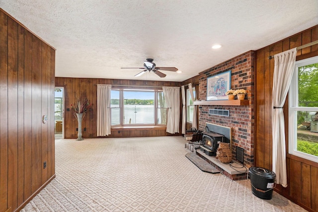 5540 Cozy Point Dr, Newaygo, MI 49337 - carpeted living room with a wood stove, plenty of natural light, wood walls, a water view, and ceiling fan